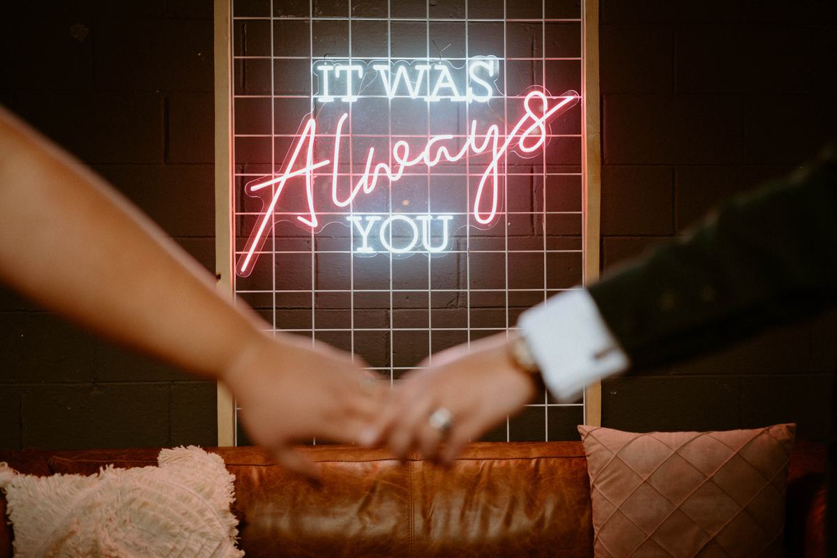 Close-up of It Was Always You neon sign behind a couple holding hands