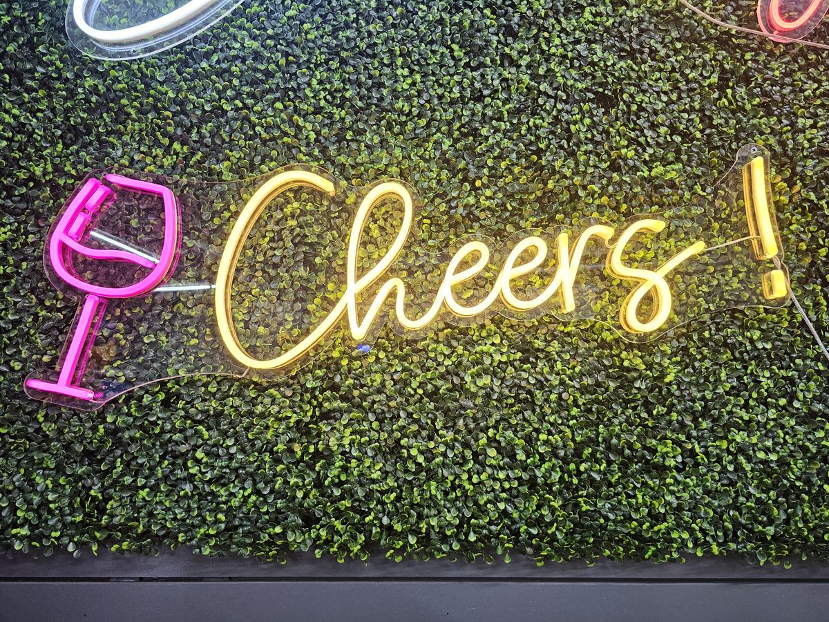 Cheers neon sign with wine glass icon on a greenery wall