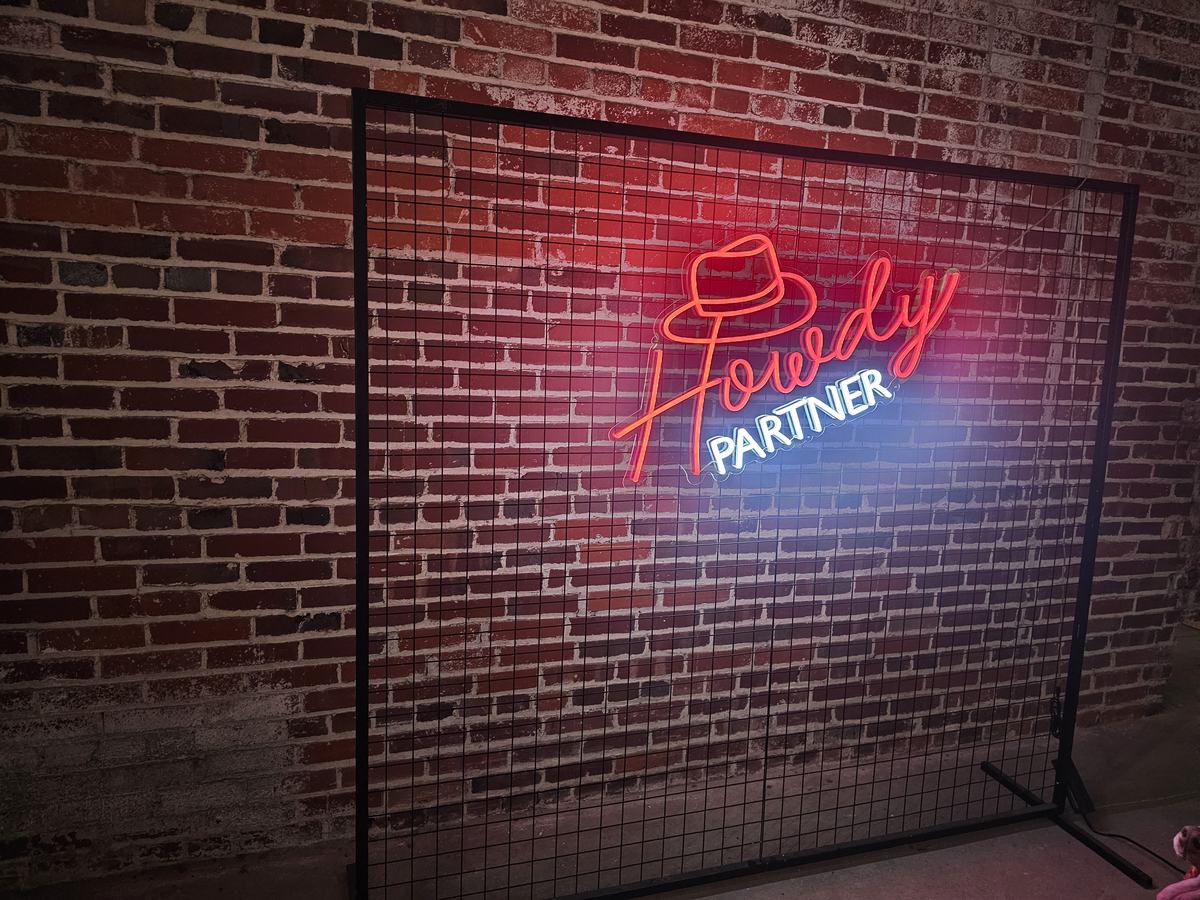 Howdy Partner neon sign with hat icon on a black square backdrop