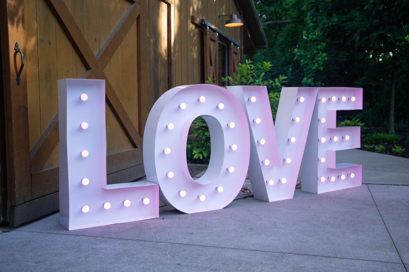 Large LOVE marquee letters glowing pink at dusk near a barn door