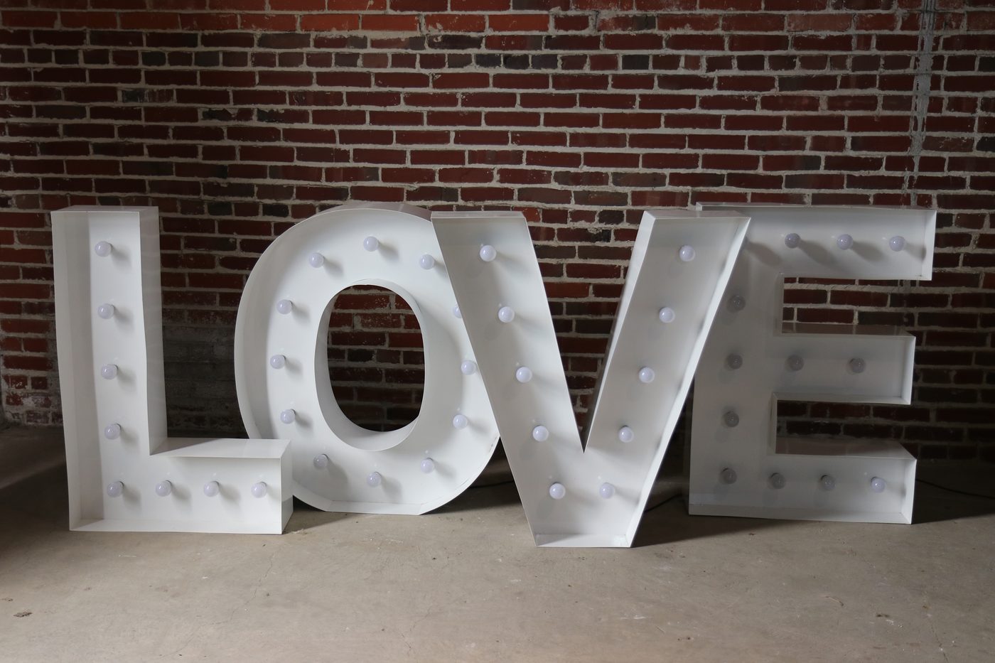 Large LOVE marquee letters unlit against a brick wall, showing the daytime look