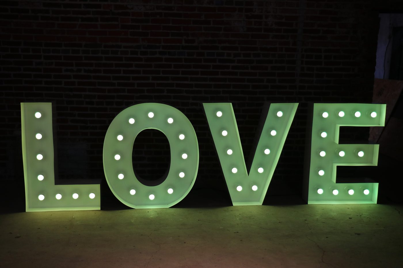 Large LOVE marquee letters glowing green against a brick wall