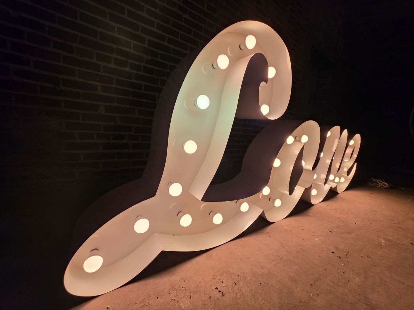 LOVE script marquee sign glowing with warm bulbs against a brick wall