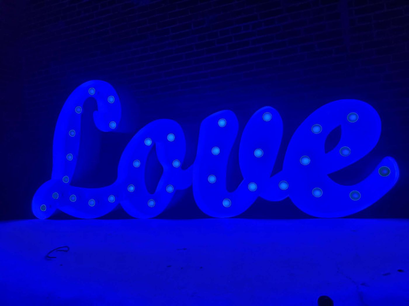 LOVE script marquee sign glowing blue against a brick wall