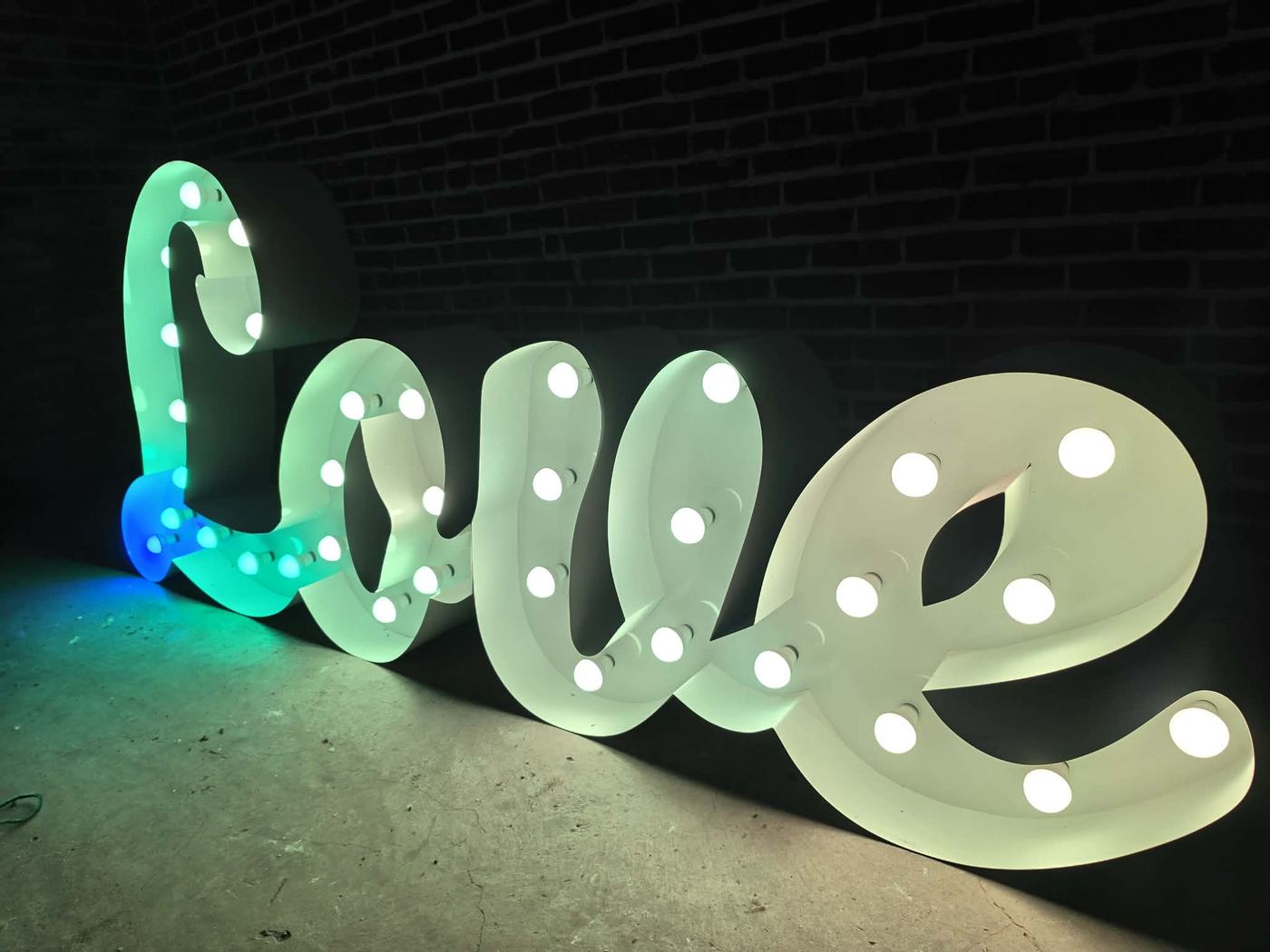 LOVE script marquee sign glowing teal and white against a brick wall