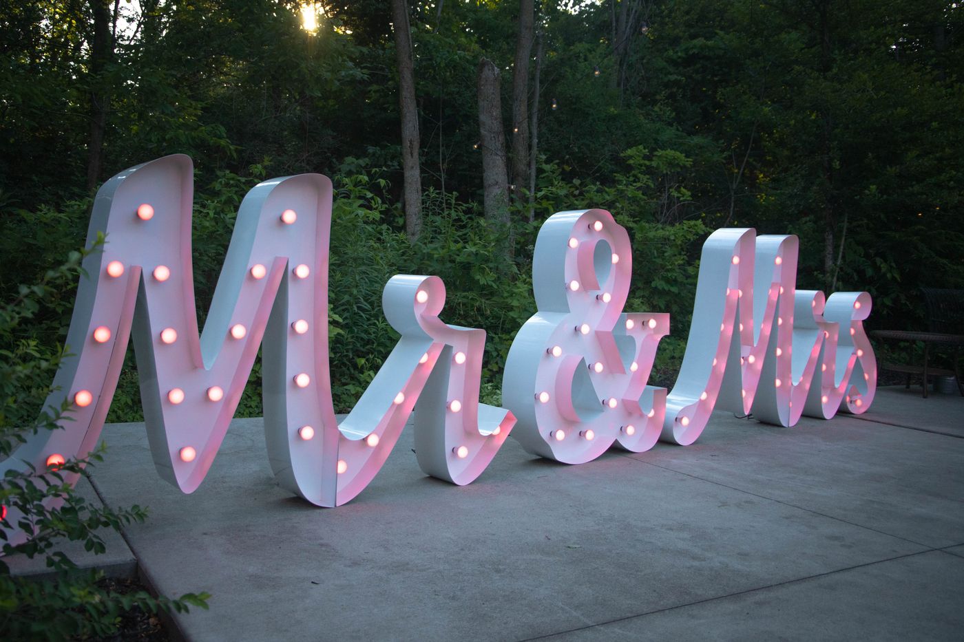 MR and MRS marquee letters glowing pink in a wooded setting at dusk