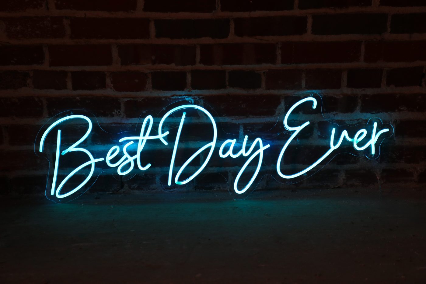 Best Day Ever script neon sign glowing teal against a brick wall