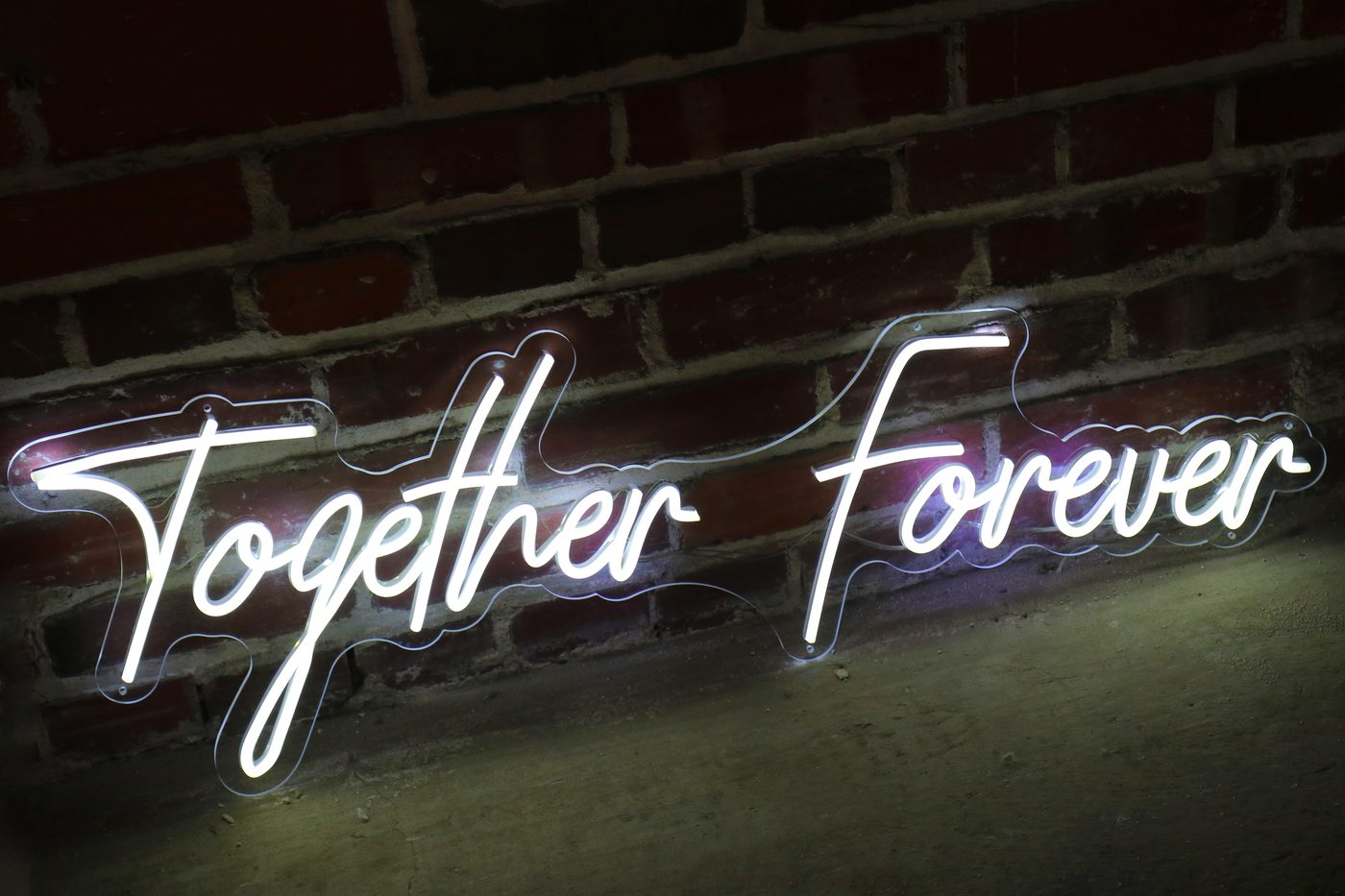 Together Forever script neon sign glowing white against a brick wall
